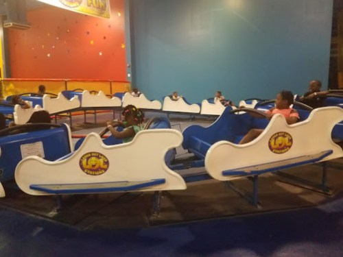 Children sitting in colorful ride cars at an indoor amusement park, ready for a fun experience.