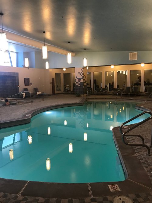 Indoor swimming pool with blue water, tiled edges, and lounge chairs, illuminated by pendant lights.