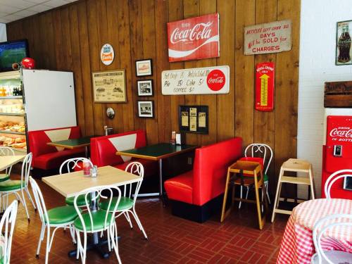 Cozy diner interior with wooden walls, vintage Coca-Cola signs, red booths, and checkered tablecloths.