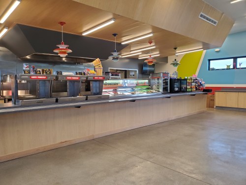 A modern cafeteria with a service counter, colorful lights, and a variety of food options displayed.