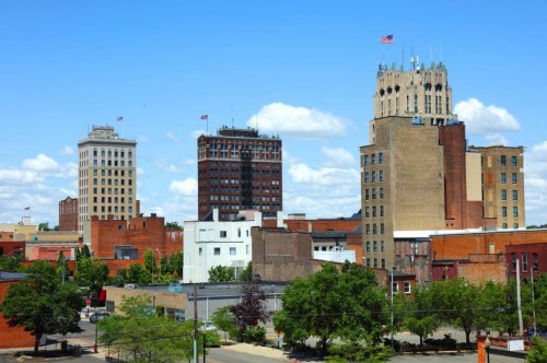 A city skyline featuring several tall buildings under a clear blue sky with scattered clouds.