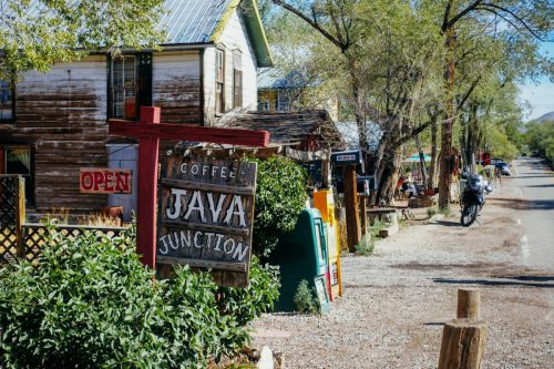 A rustic coffee shop sign reading "Java Junction" with a charming street scene and greenery in a small town.
