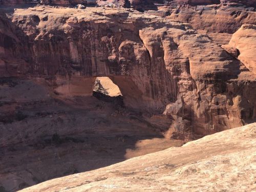 A natural rock arch stands amidst rugged, reddish-brown cliffs in a desert landscape.