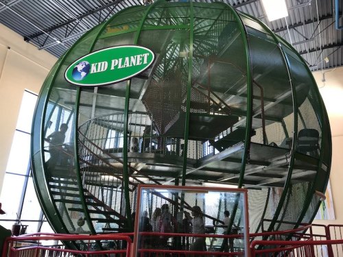 A large green play structure shaped like a globe, with children playing inside and on various levels.