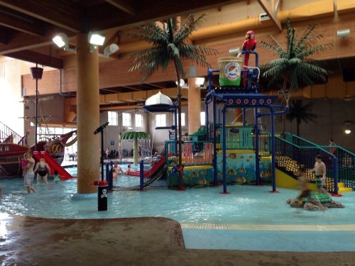 Indoor water park featuring slides, play structures, and palm trees, with children playing in the shallow water.