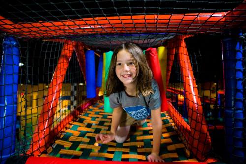 A smiling child crawls through a colorful play structure with nets and soft barriers.
