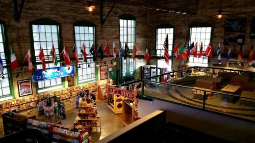 Interior of a gift shop with flags hanging from the ceiling and shelves filled with souvenirs and tourist information.