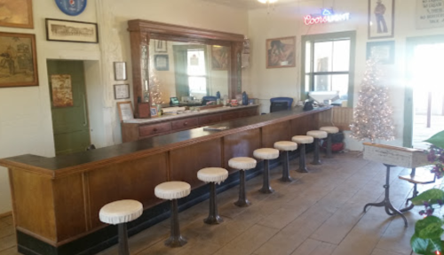 A vintage bar with a wooden counter, stools, and decorative wall art, featuring a mirror and a small Christmas tree.