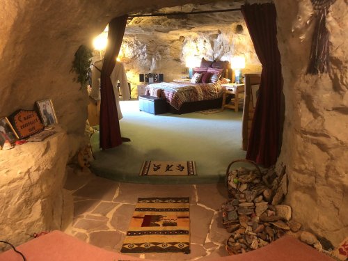 Cozy cave interior with a bed, decorative rugs, and warm lighting, creating a unique living space.
