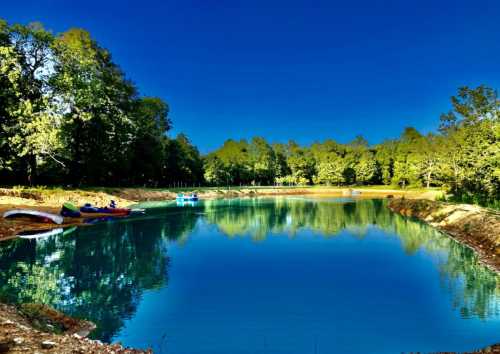 A serene lake surrounded by lush trees, reflecting the clear blue sky and colorful kayaks on the water.