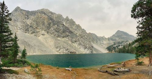A serene lake surrounded by rocky mountains and pine trees, with a cloudy sky overhead.
