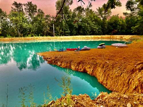 A serene pond surrounded by trees, with colorful kayaks and inflatable boats on the shore.