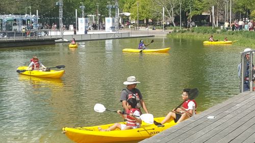 People kayaking in yellow kayaks on a calm waterway, with greenery and a boardwalk in the background.