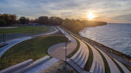 A scenic view of a park by the water at sunset, featuring pathways and steps leading to the shoreline.