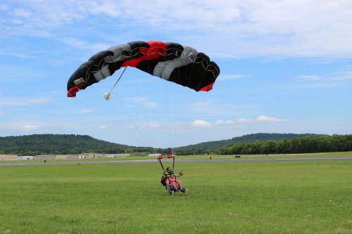 A person landing with a parachute on a grassy field, surrounded by hills and a clear blue sky.