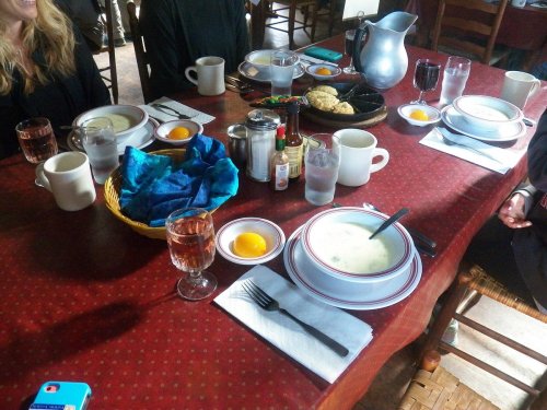 A dining table set with plates, glasses, and a basket of food, featuring eggs and a pitcher, in a cozy setting.