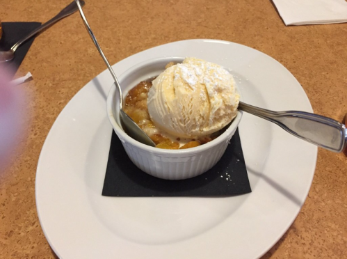 A ramekin of warm dessert topped with a scoop of vanilla ice cream and a dusting of powdered sugar.