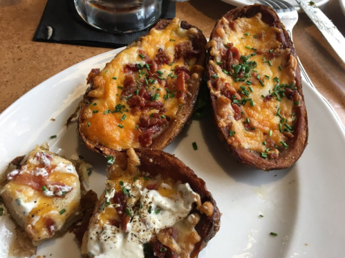 A plate of loaded potato skins topped with cheese, bacon, and chives, with a side of sour cream.