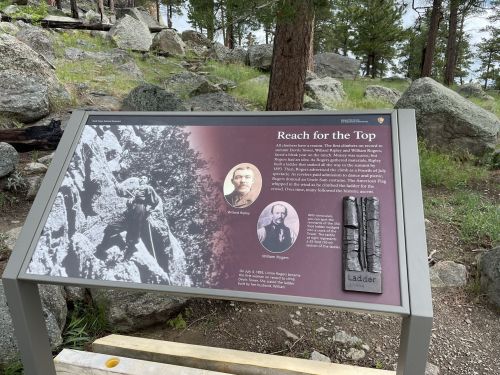 Sign titled "Reach for the Top" featuring historical photos and text about climbing and exploration in a natural setting.