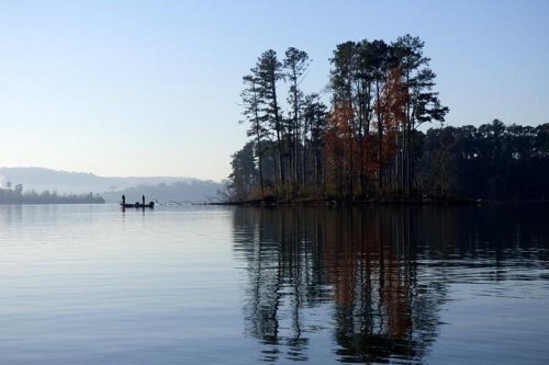 A serene lake scene at dawn, featuring an island with trees and two people in a boat, reflecting on the water.