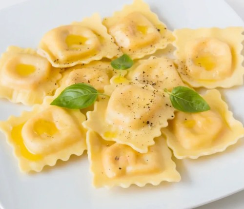 A plate of ravioli filled with yellow filling, garnished with basil and black pepper.