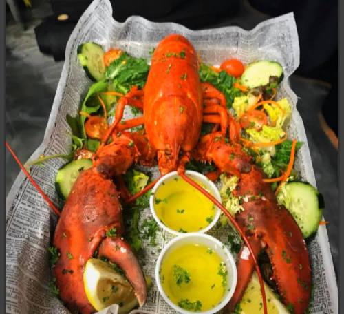 A platter featuring a whole lobster and two lobster claws, garnished with salad and served with dipping sauces.