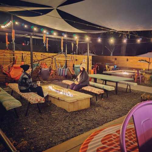 Cozy outdoor seating area with hammocks, string lights, and a fire pit, creating a warm, inviting atmosphere.