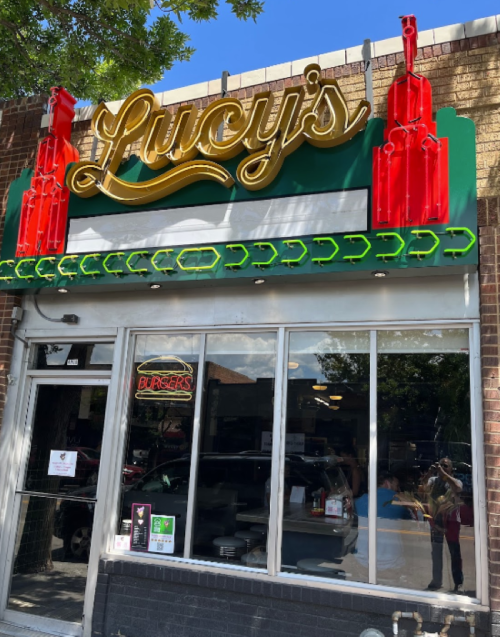 Sign for "Lucy's" restaurant featuring red gun decorations and a large window displaying the interior.
