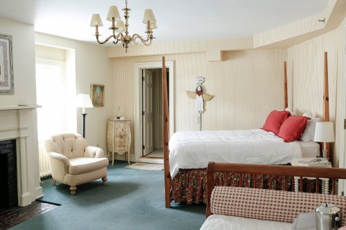 Cozy bedroom featuring a four-poster bed, armchair, chandelier, and soft color palette with floral accents.