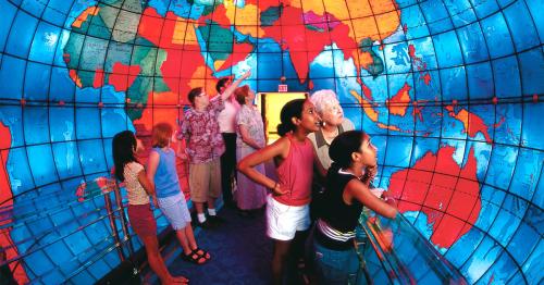A diverse group of people explores a colorful globe mural, pointing and observing the world map around them.