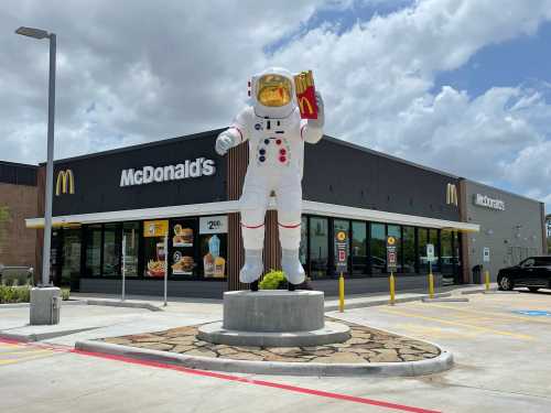 A large astronaut statue holding fries stands in front of a McDonald's restaurant under a cloudy sky.