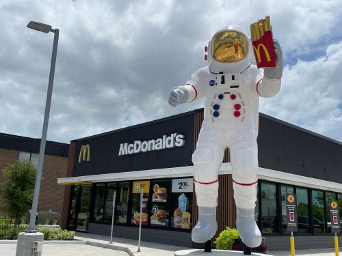A large astronaut statue holding fries stands in front of a McDonald's restaurant under a cloudy sky.