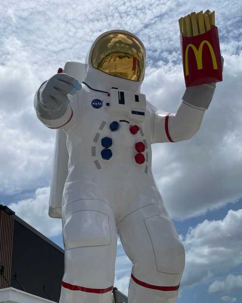 A giant astronaut statue holding a container of McDonald's fries against a cloudy sky.