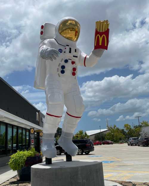 A large astronaut statue holding a French fry container outside a McDonald's restaurant under a cloudy sky.