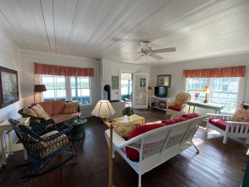 Bright, airy living room with white walls, wooden floors, and cozy furniture, featuring large windows and a view outside.