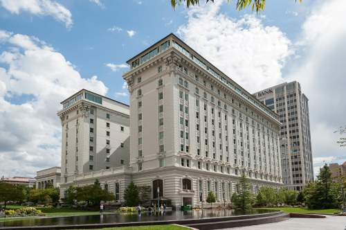 A large, elegant building with a classic facade, surrounded by greenery and under a partly cloudy sky.