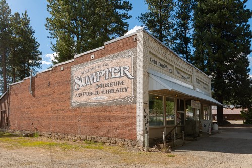 A brick building with a mural reading "Welcome to the Sumpter Museum and Public Library" surrounded by trees.