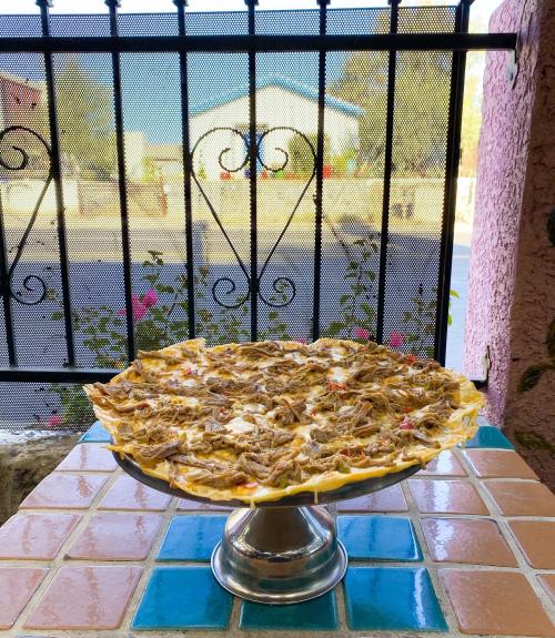A large, topped pizza on a silver stand, with a decorative background of a window and colorful tiles.