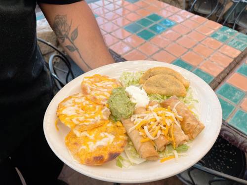 A plate of Mexican food featuring cheese-topped tortillas, guacamole, sour cream, and rolled tacos on a bed of lettuce.