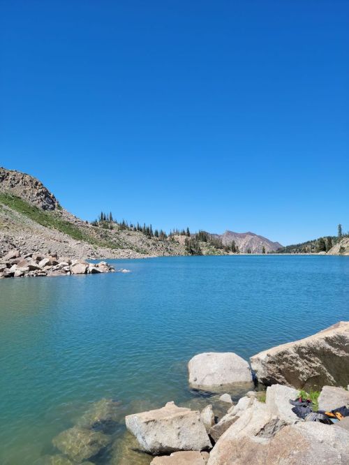 A serene lake surrounded by rocky shores and green hills under a clear blue sky.