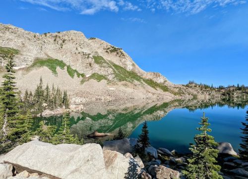 A serene mountain lake reflecting rocky cliffs and trees under a clear blue sky.