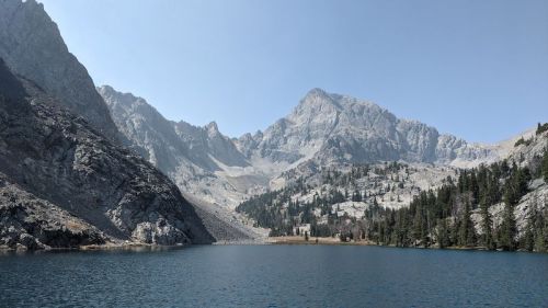 A serene mountain lake surrounded by rugged peaks and lush greenery under a clear blue sky.