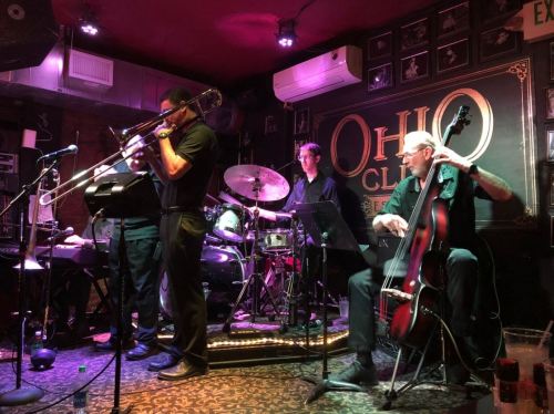 A jazz band performs on stage at the Ohio Club, featuring a trombonist, drummer, and bassist.