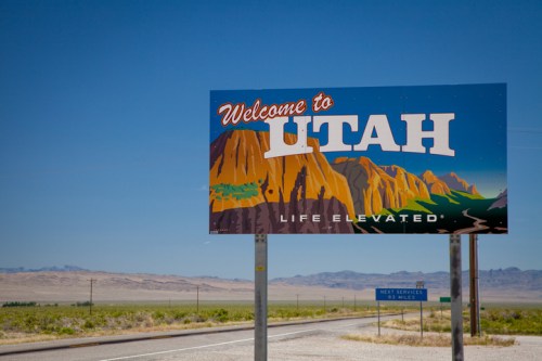 A colorful "Welcome to Utah" sign featuring mountains and the slogan "Life Elevated" against a clear blue sky.
