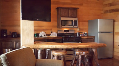 Cozy cabin kitchen with wooden accents, stainless steel appliances, and a rustic bar with stools.