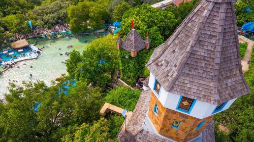 Aerial view of a water park featuring a tower, lush greenery, and people enjoying the water.