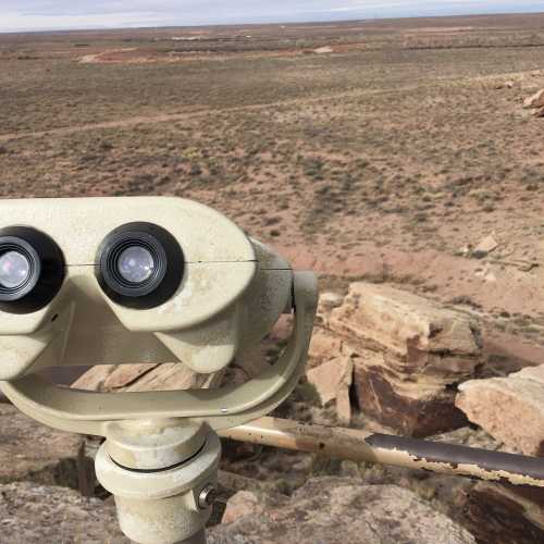 A pair of binoculars mounted on a stand, overlooking a vast, arid landscape with rocky terrain and distant hills.