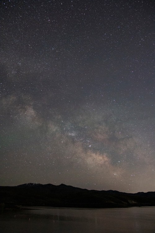 A starry night sky filled with the Milky Way over a calm lake and distant mountains.