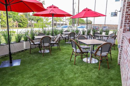 Outdoor dining area with red umbrellas, tables, and chairs on green grass.