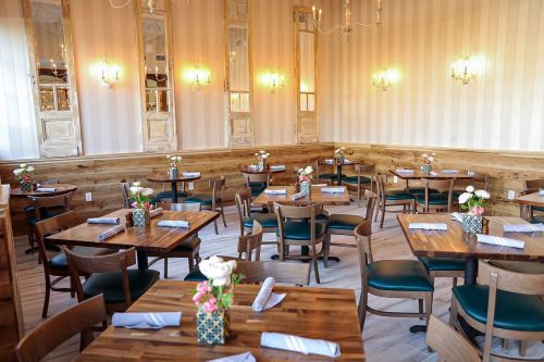 A cozy restaurant interior with wooden tables, green chairs, and floral centerpieces, featuring soft lighting and elegant decor.